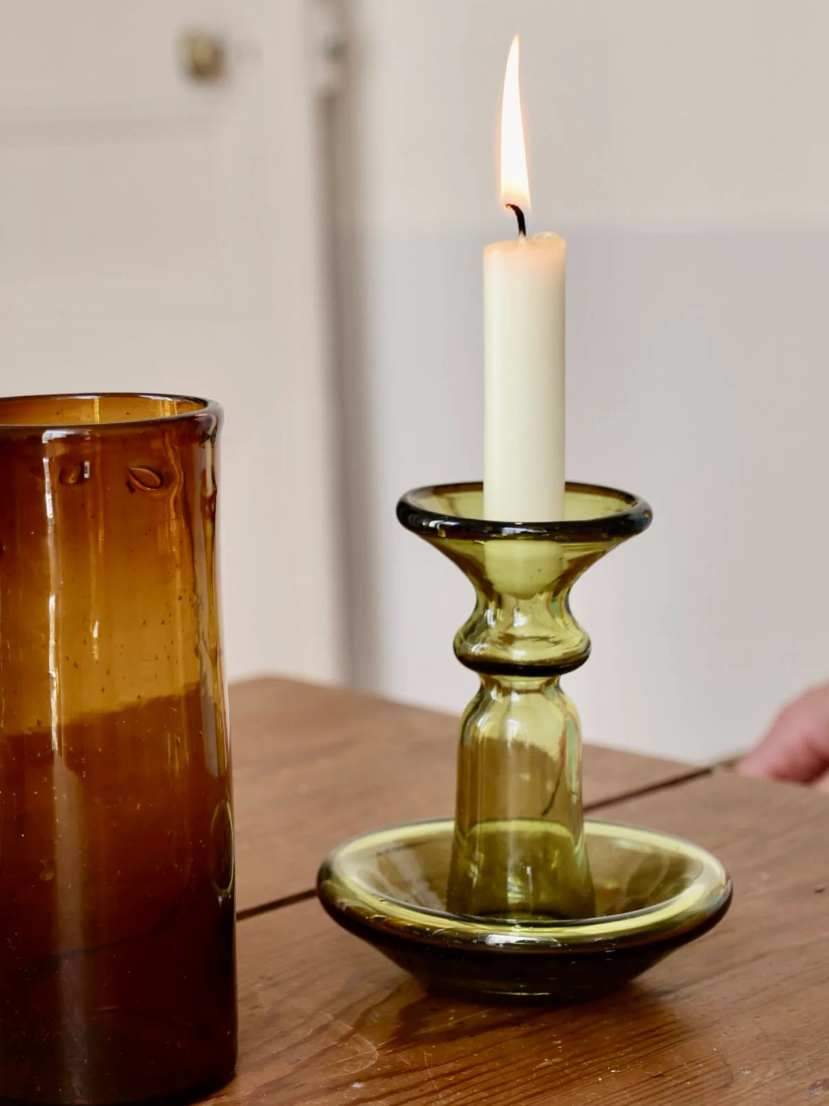 Candle in a green mouth-blown glass candlestick holder on a wooden surface with a blurred background