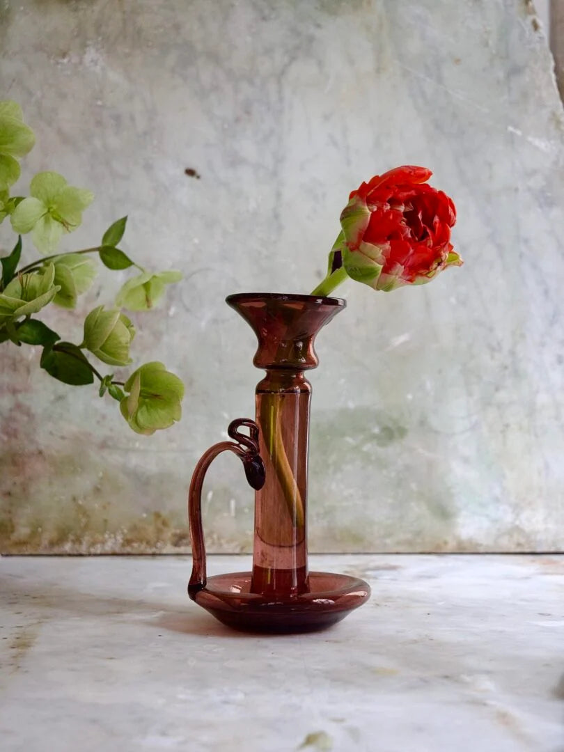 Brown and raspberry hand-blown glass vase with a red flower against a textured white background