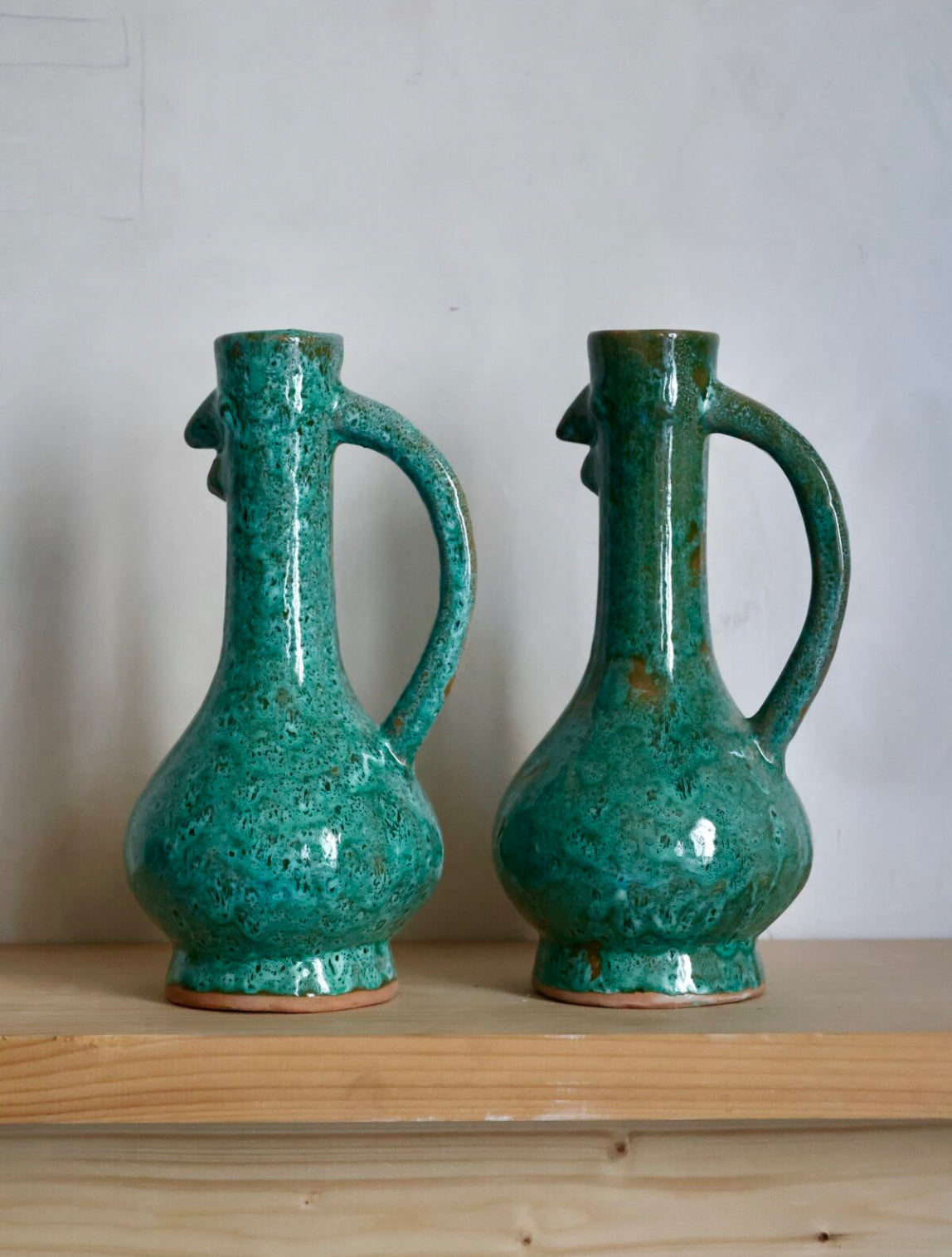 Two turquoise ceramic rustic French chicken-shaped vases with handles on a wooden surface and light gray background