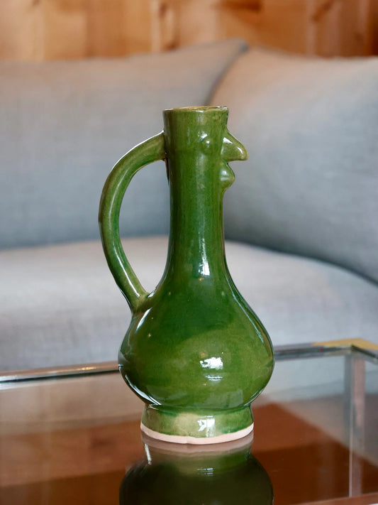 Green ceramic chicken-shaped vase with a handle on a reflective surface