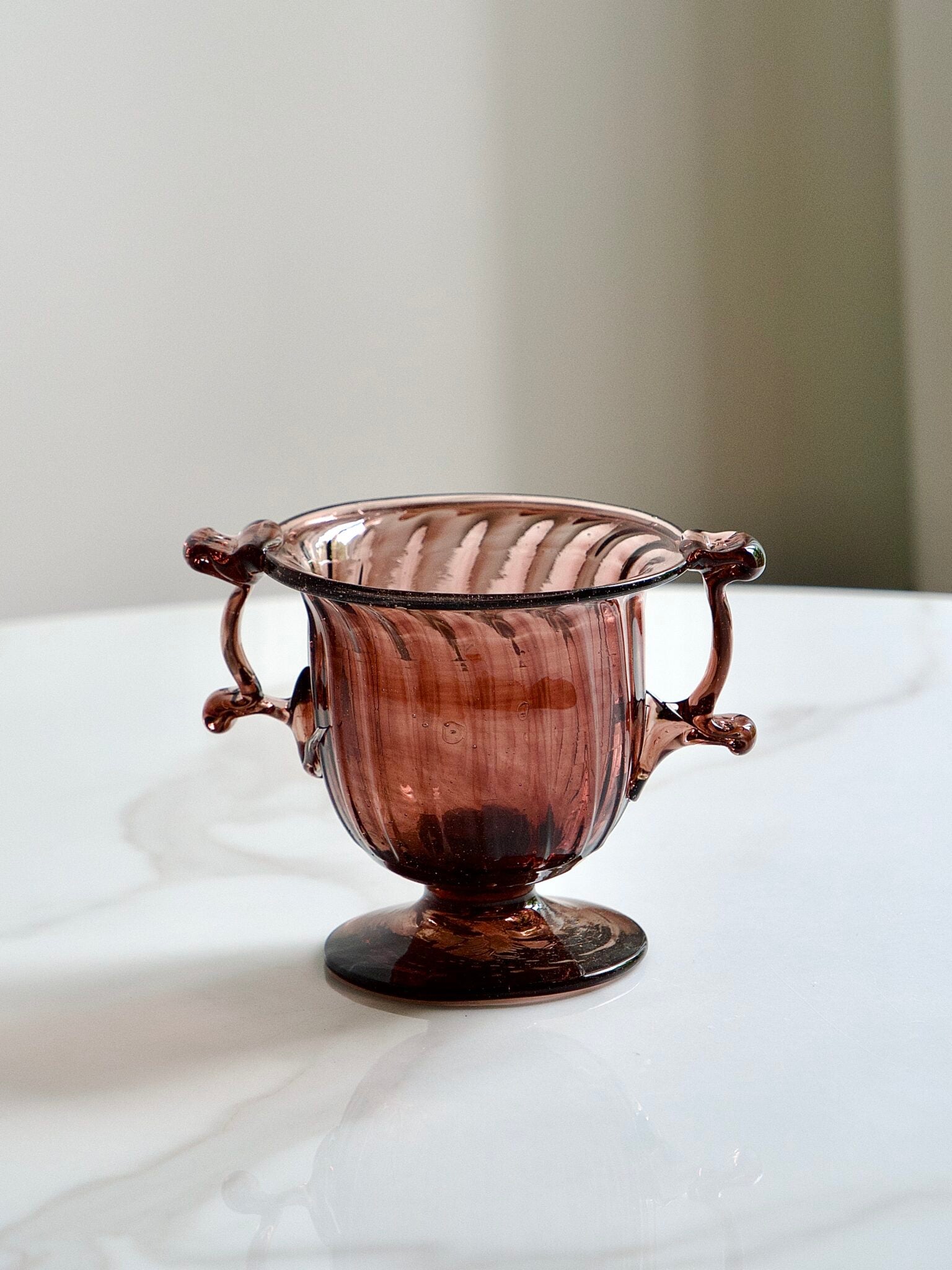 Decorative handmade raspberry recycled glass bowl with handles on a marble surface
