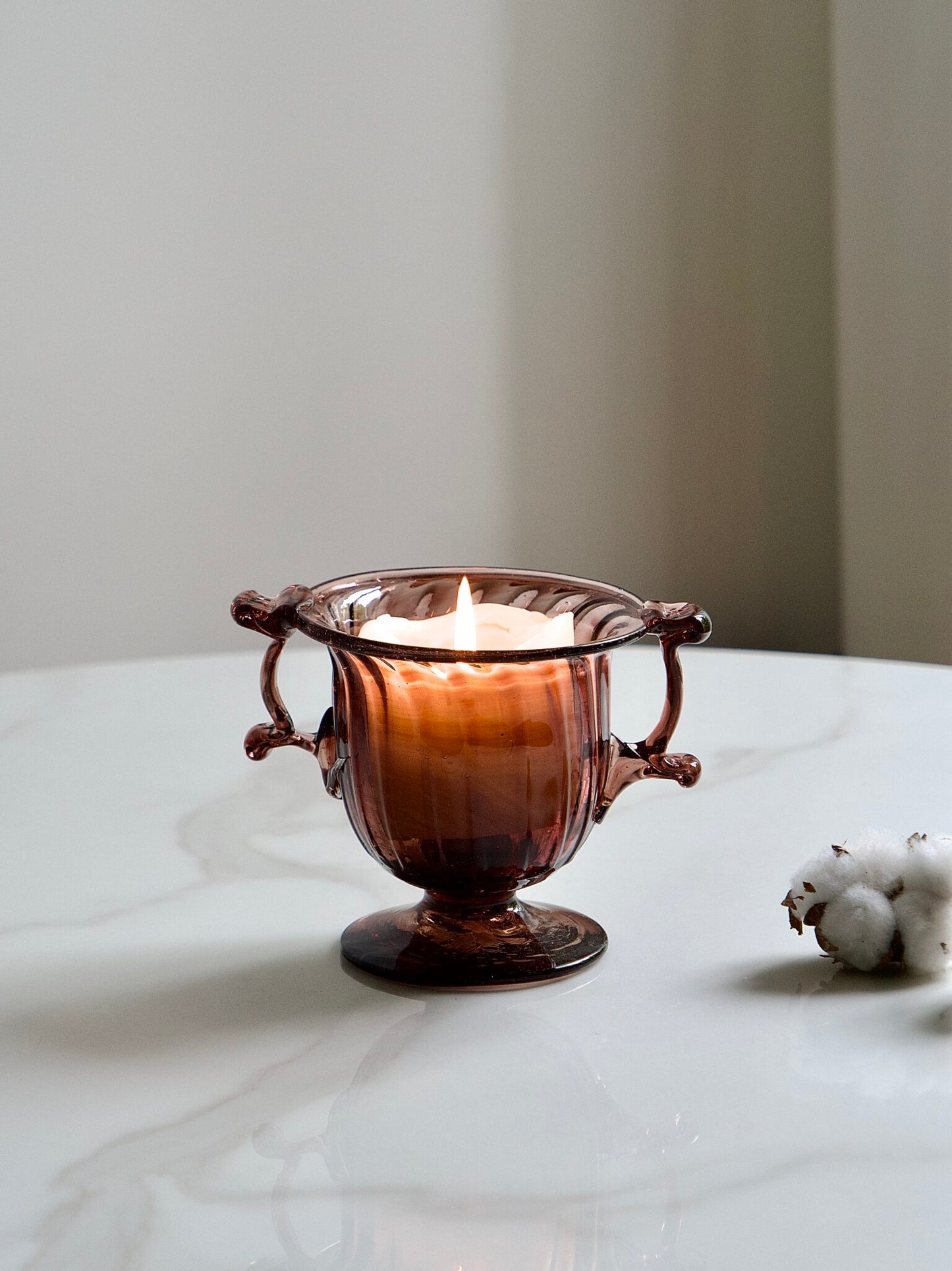 Decorative artisan mouth-blown framboise glass bowl or candle holder with a candle on a marble surface