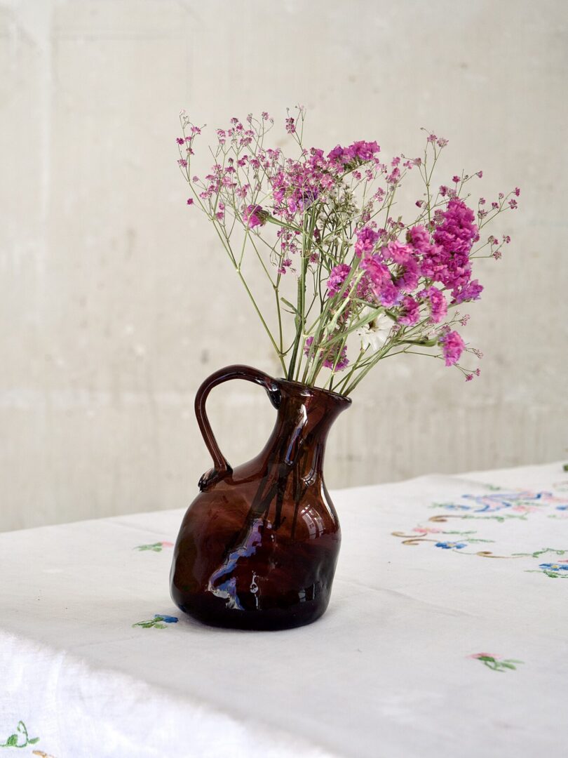 Brown elegant tilted pitcher with pink flowers on a white tablecloth.