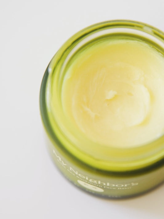 Close-up of a green glass jar with the 'My Neighbors' Rose and Sea buckthorn tallow balm inside, on a white background