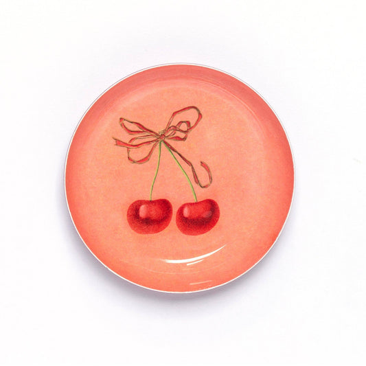 A round peach pink enamel tray with a cherry design in the center, depicted with a red bow and two cherry fruits.