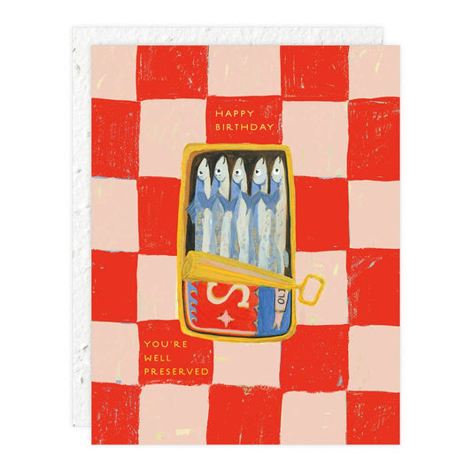 A birthday card with a red and white checkered background featuring a cartoon illustration of sardines in a can with the text 'Happy Birthday' and 'You're well preserved'.