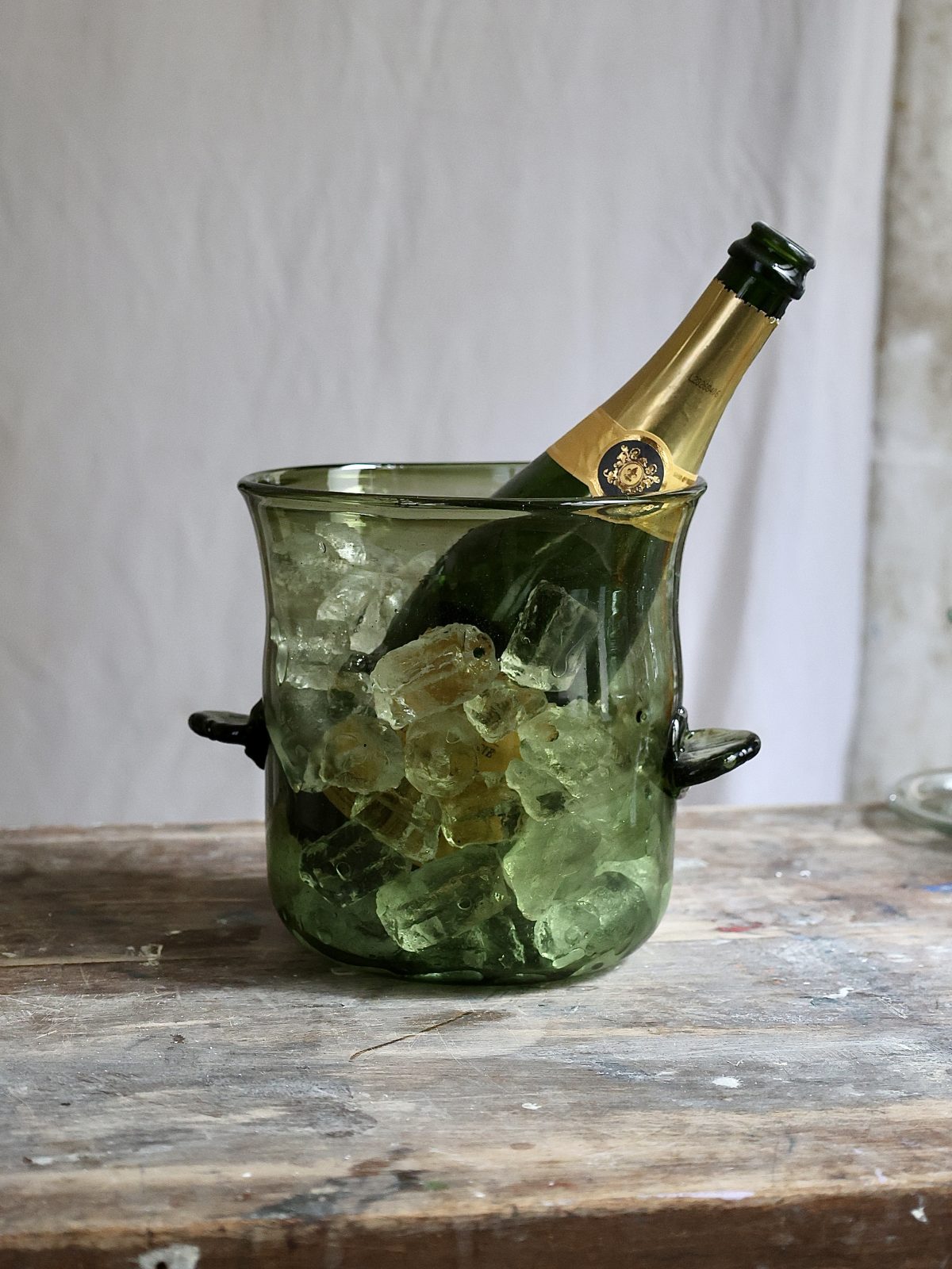 Green glass ice bucket with a bottle of champagne on a wooden surface.