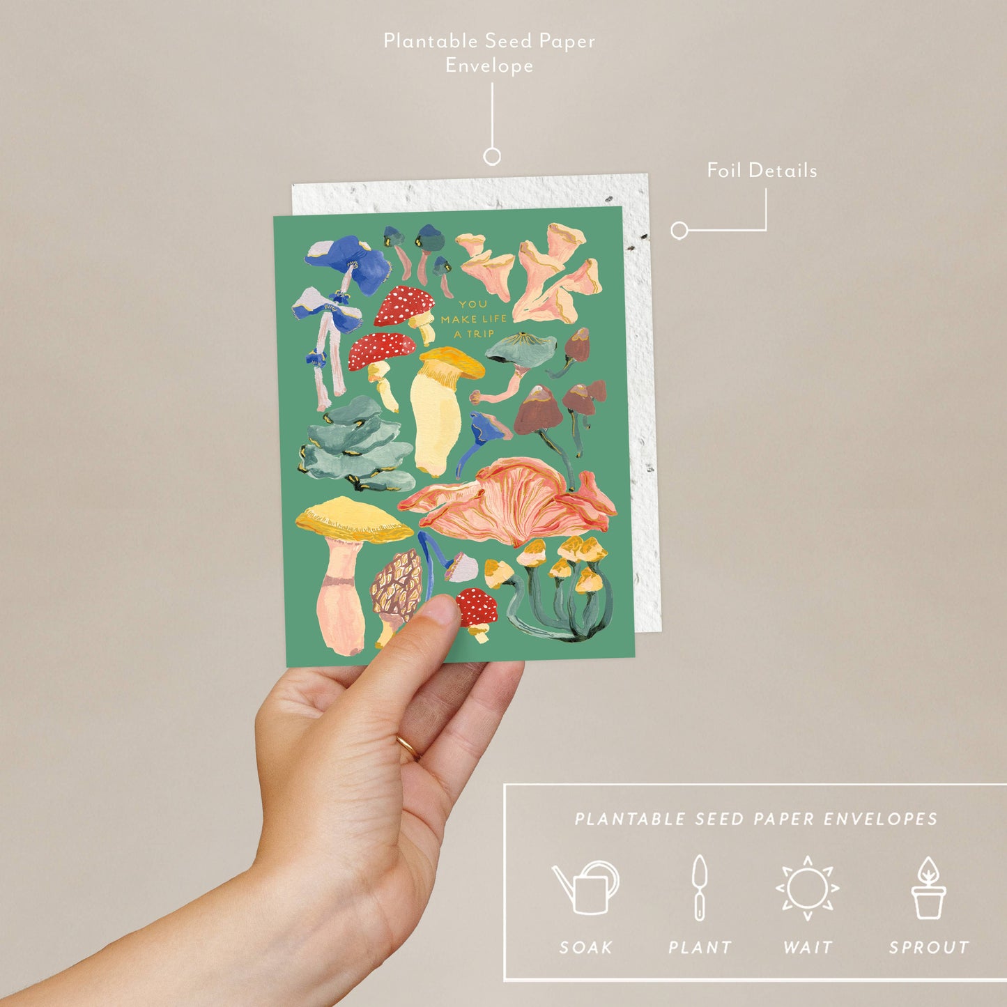 A hand holding a Greeting card with colorful mushroom illustrations and text 'You make life a trip' on a green background, accompanied by a plantable seed paper envelope with eco-friendly packaging details.