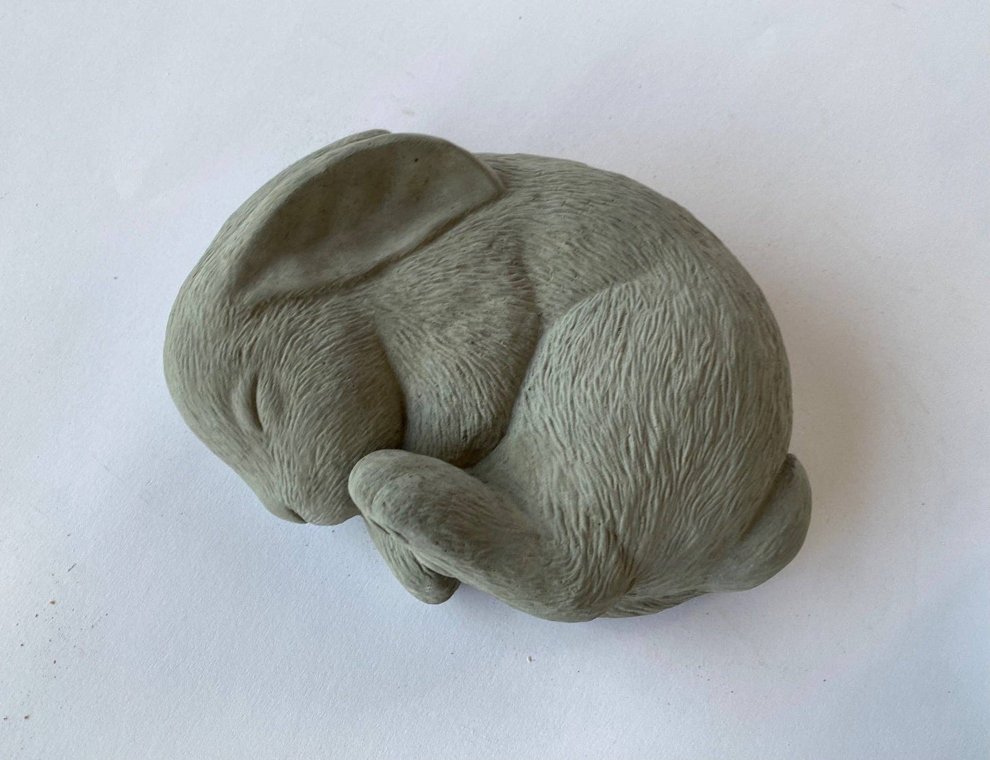 A gray concrete sculpture of a sleeping bunny in a curled position, for a peaceful garden decor.