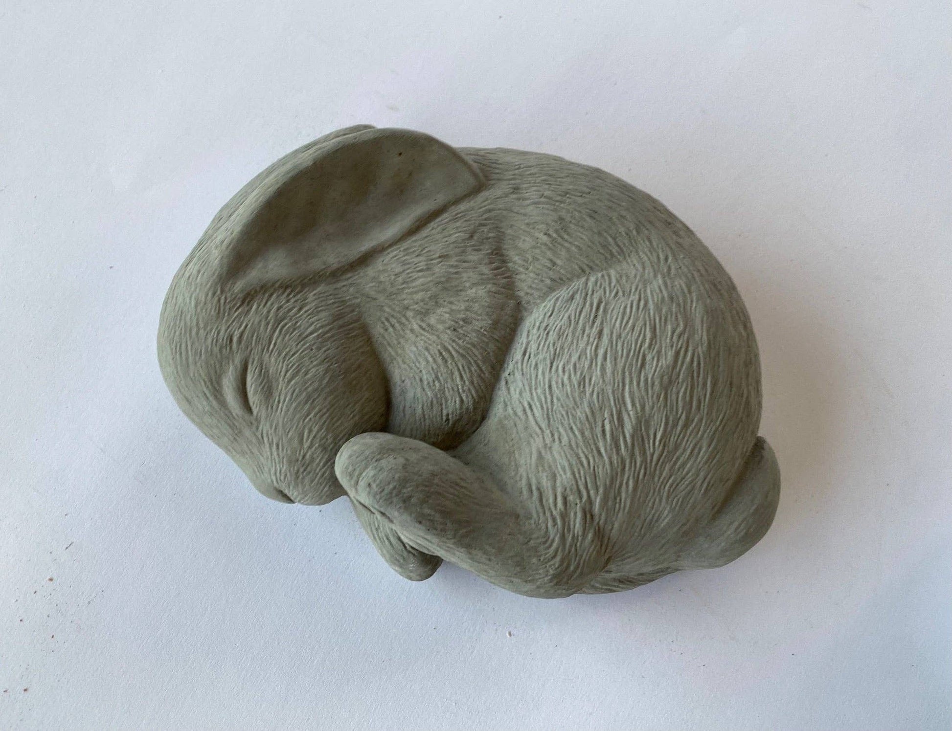 A gray concrete sculpture of a sleeping bunny in a curled position, for a peaceful garden decor.