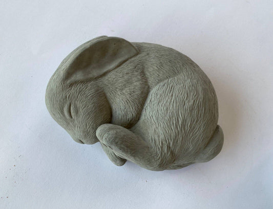 A gray concrete sculpture of a sleeping bunny in a curled position, for a peaceful garden decor.