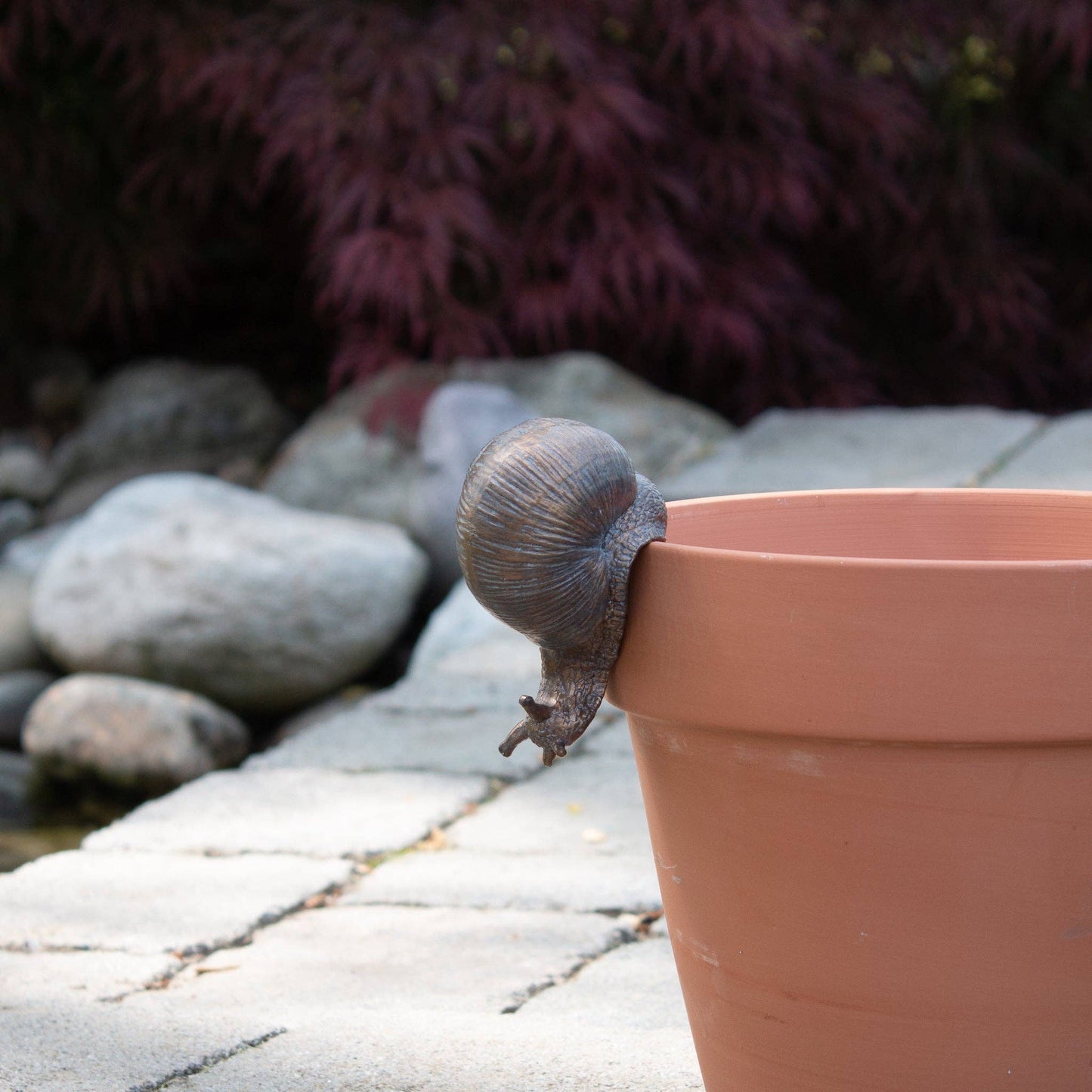 A decorative garden snail-shaped pot hugger placed on the edge of a terracotta pot.