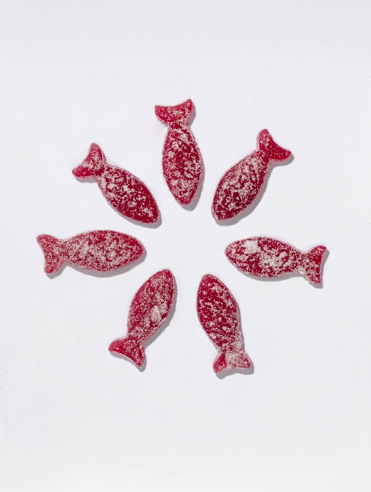 Red fish-shaped swedish candies with white sprinkles on a white background