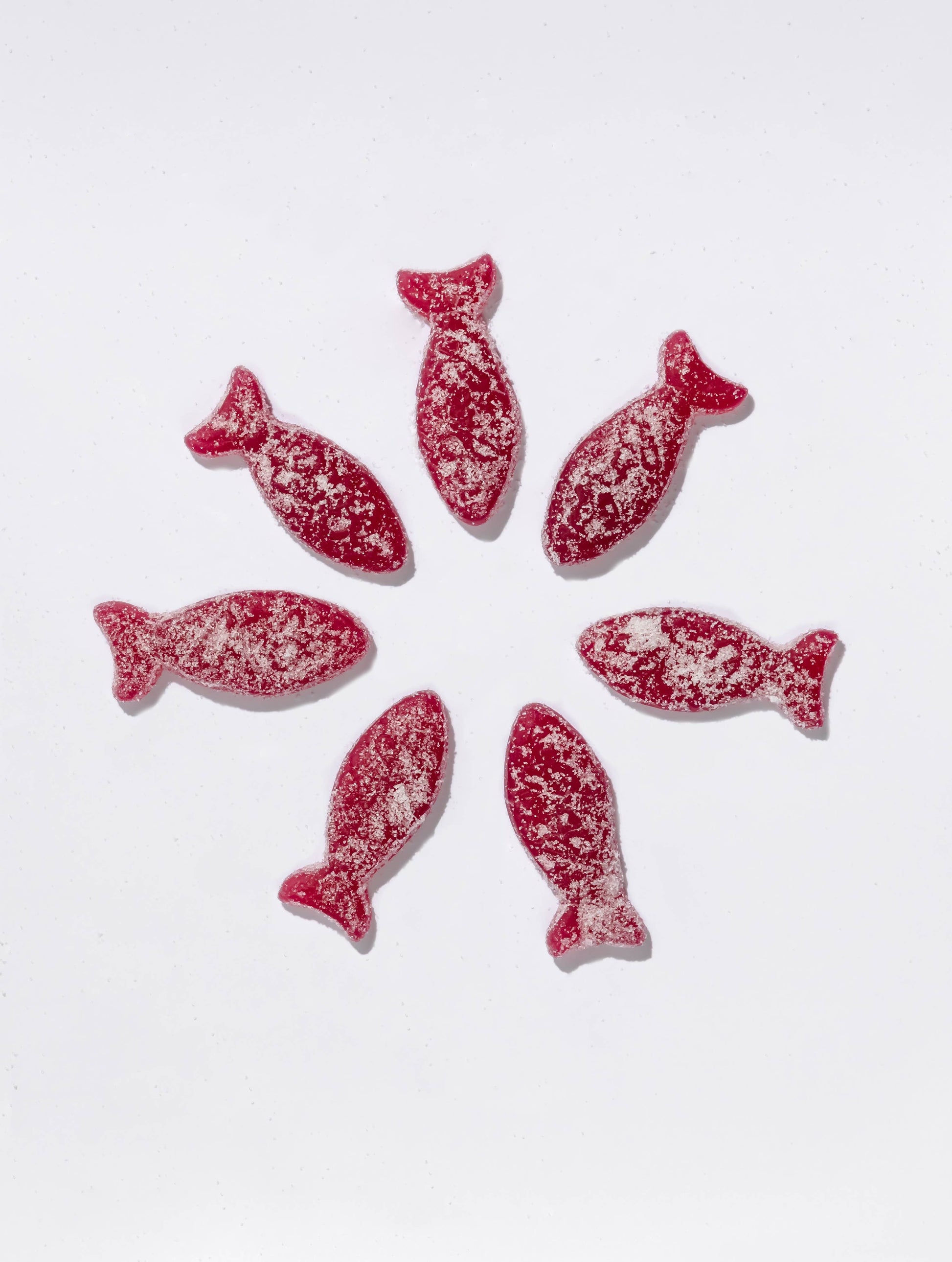 Red fish-shaped swedish candies with white sprinkles on a white background