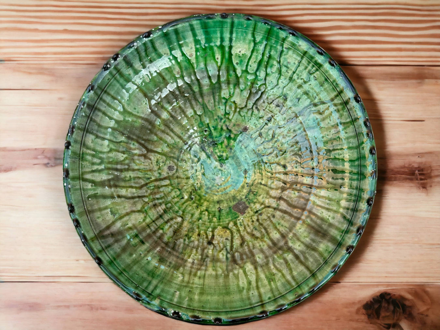 A green glazed ceramic plate with varying shades and textures, indicative of handmade tamegroute moroccan pottery, viewed from above.