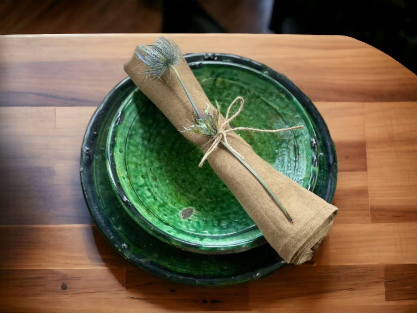 A set of two green glazed ceramic plates with varying shades and textures, indicative of handmade tamegroute moroccan pottery, displayed with a napkin and a flower on a wooden table.