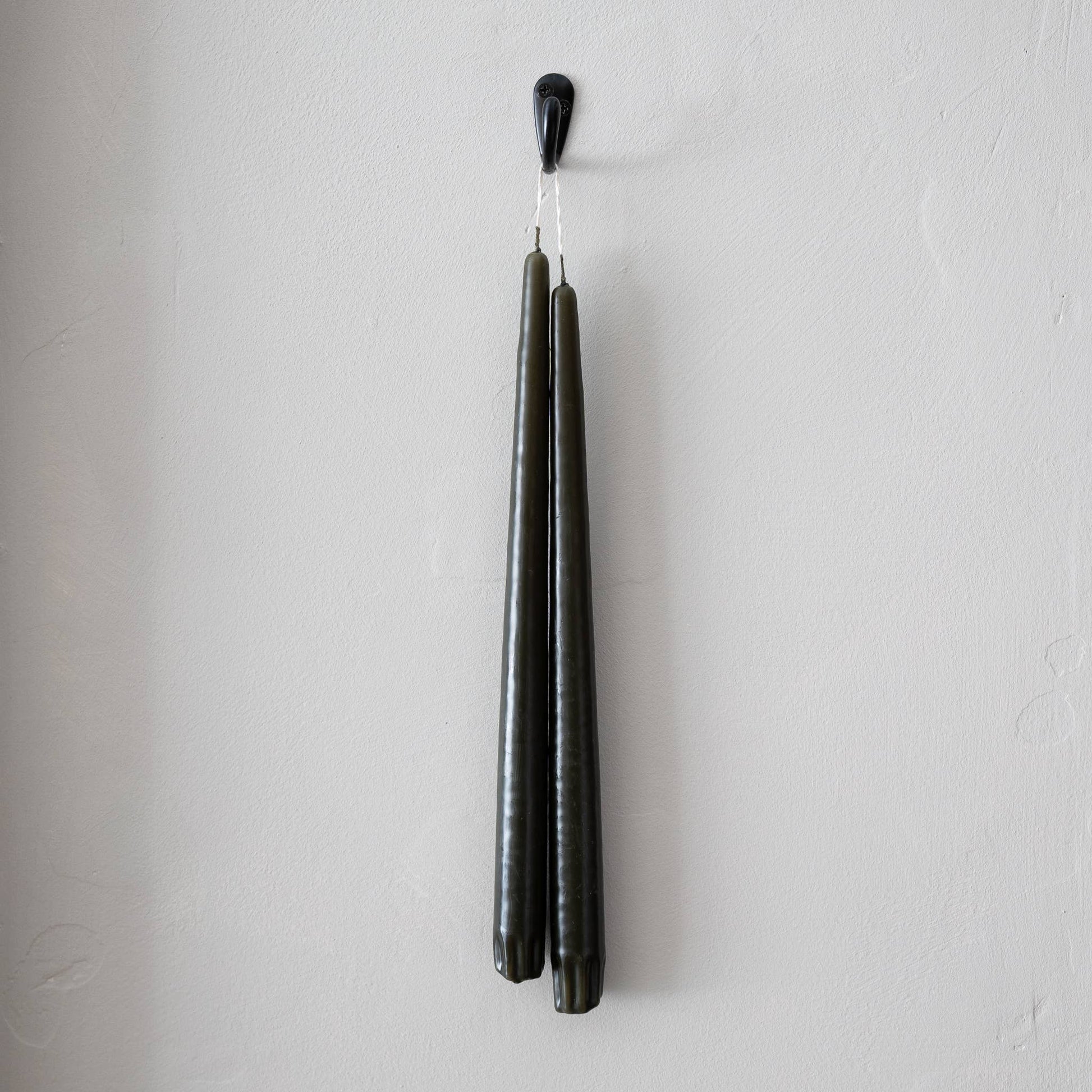 A pair of olive green taper candles hanging from a holder, with wicks hanging downwards.