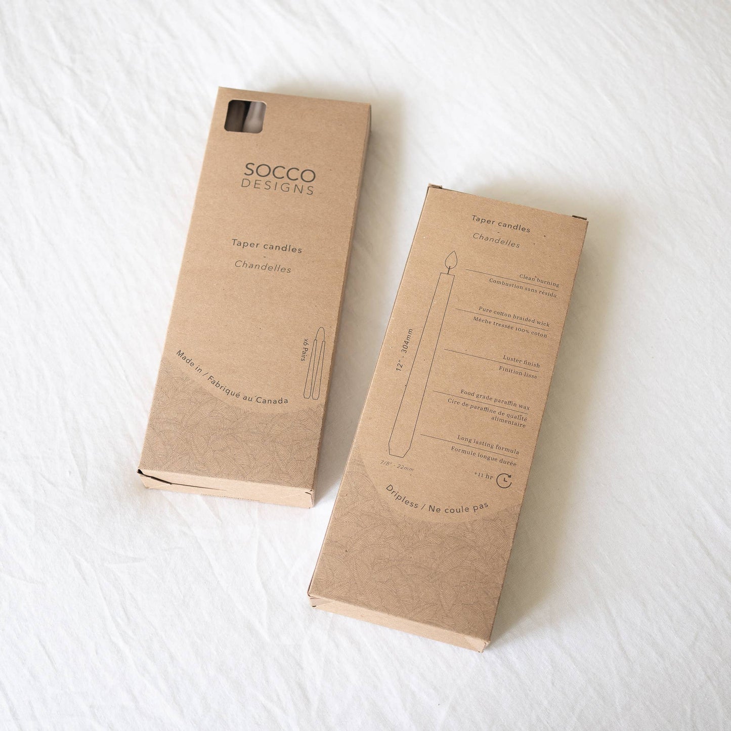Box of taper candles from Socco Designs with details: handmade in Canada, clean and dripless burning that lasts approximately 11 hours, Sold as pairs, Dimensions 12", 7/8" Base, fits any standard taper holder, Unscented, Pure Cotton Braided Wick, Luster finish, Food Grade Paraffin Wax
