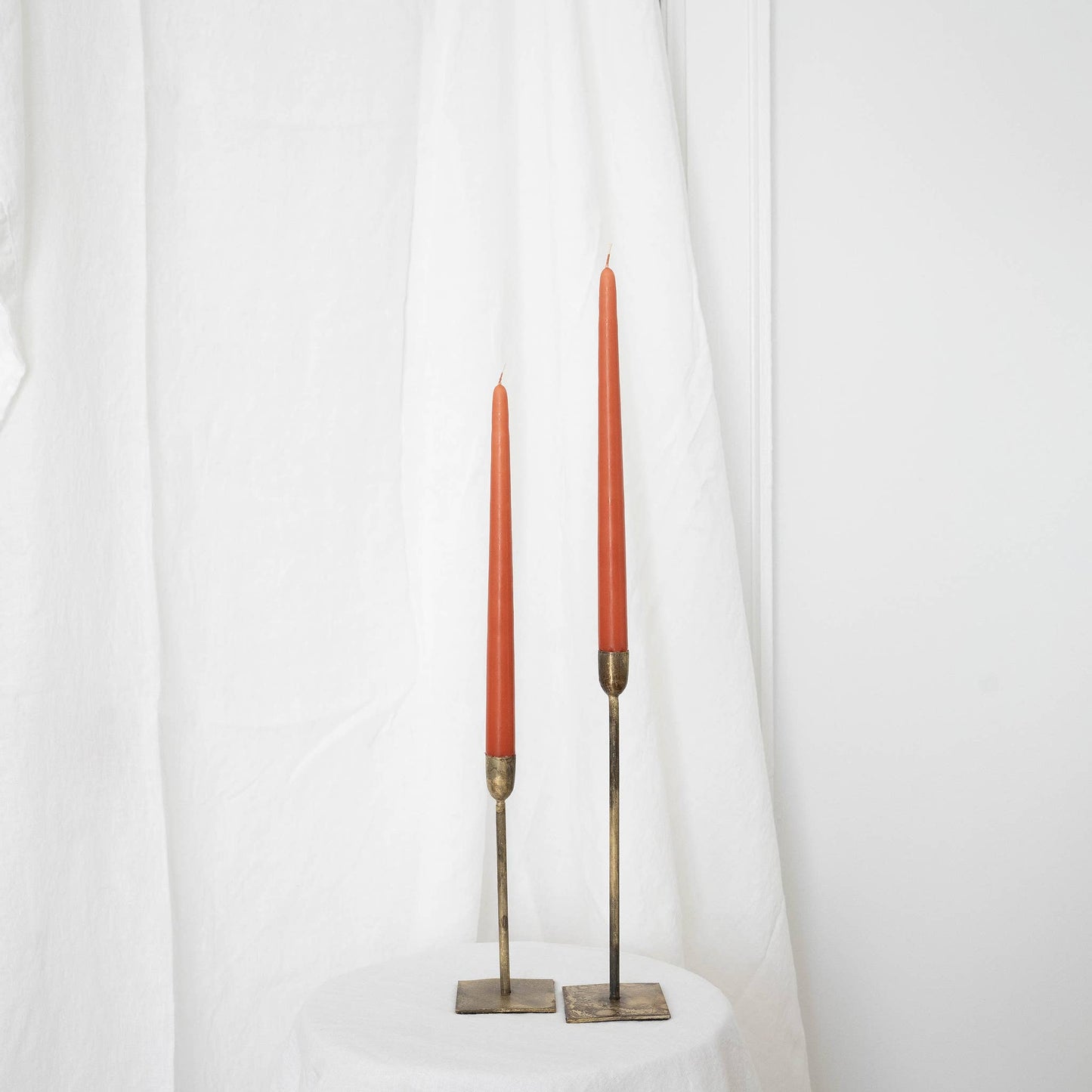 A pair of terracotta taper candles in taper holders on a white draped wall.