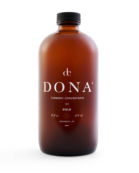 A 16oz glass bottle of Dona Turmeric Concentrate, perfect for golden lattes, with a label displaying the product name and ingredients.