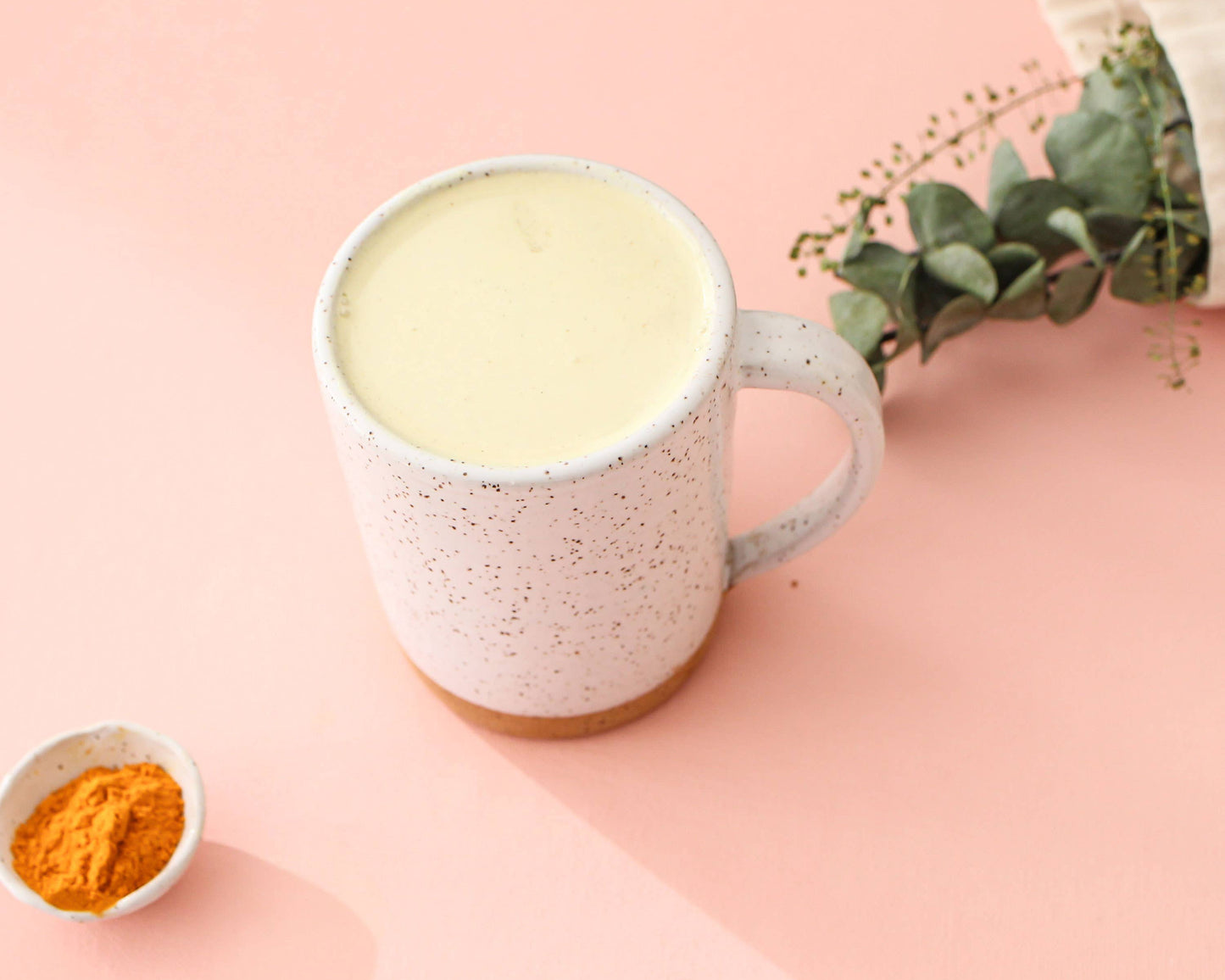 Mug of a golden latte with turmeric powder on a pink background