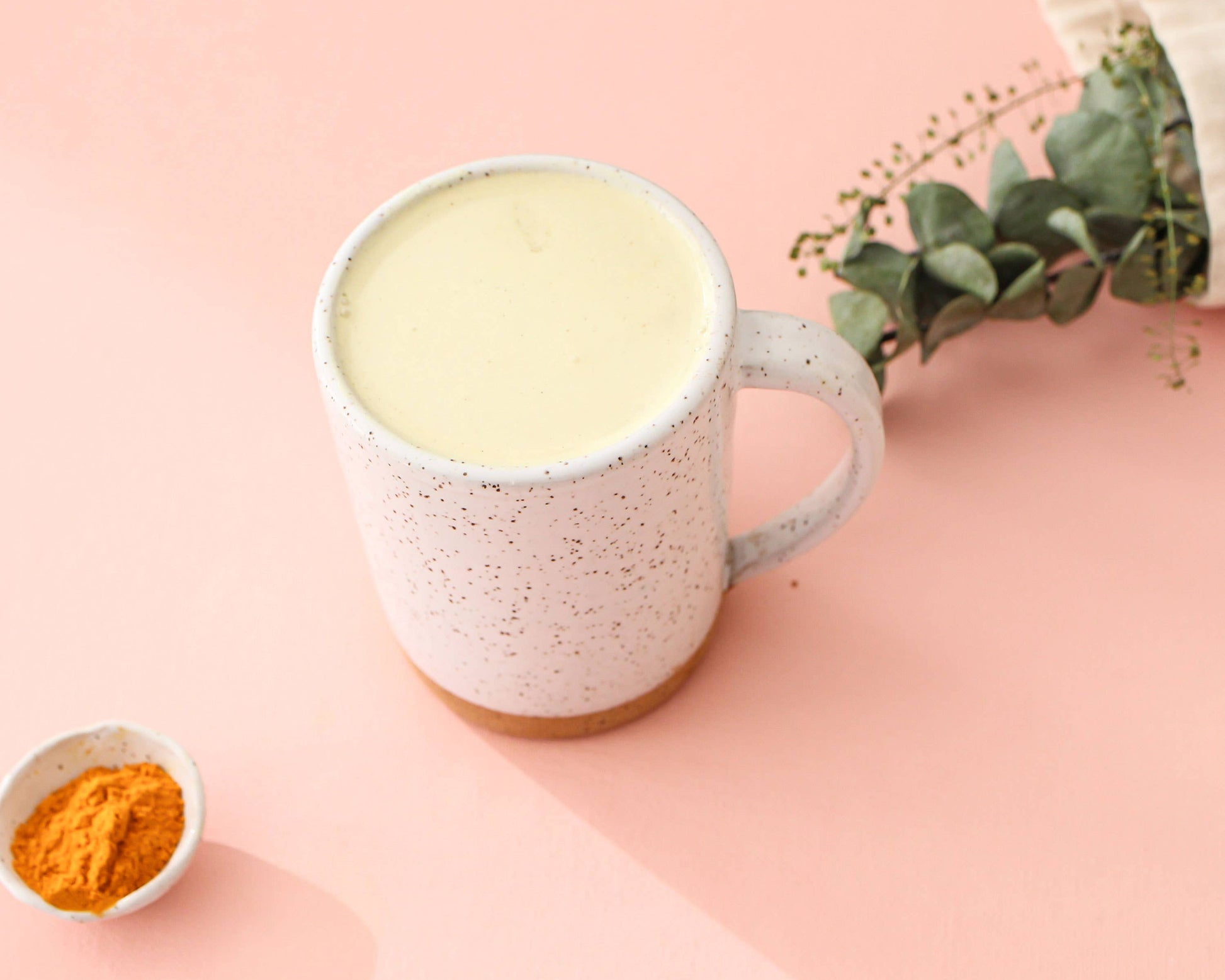 Mug of a golden latte with turmeric powder on a pink background