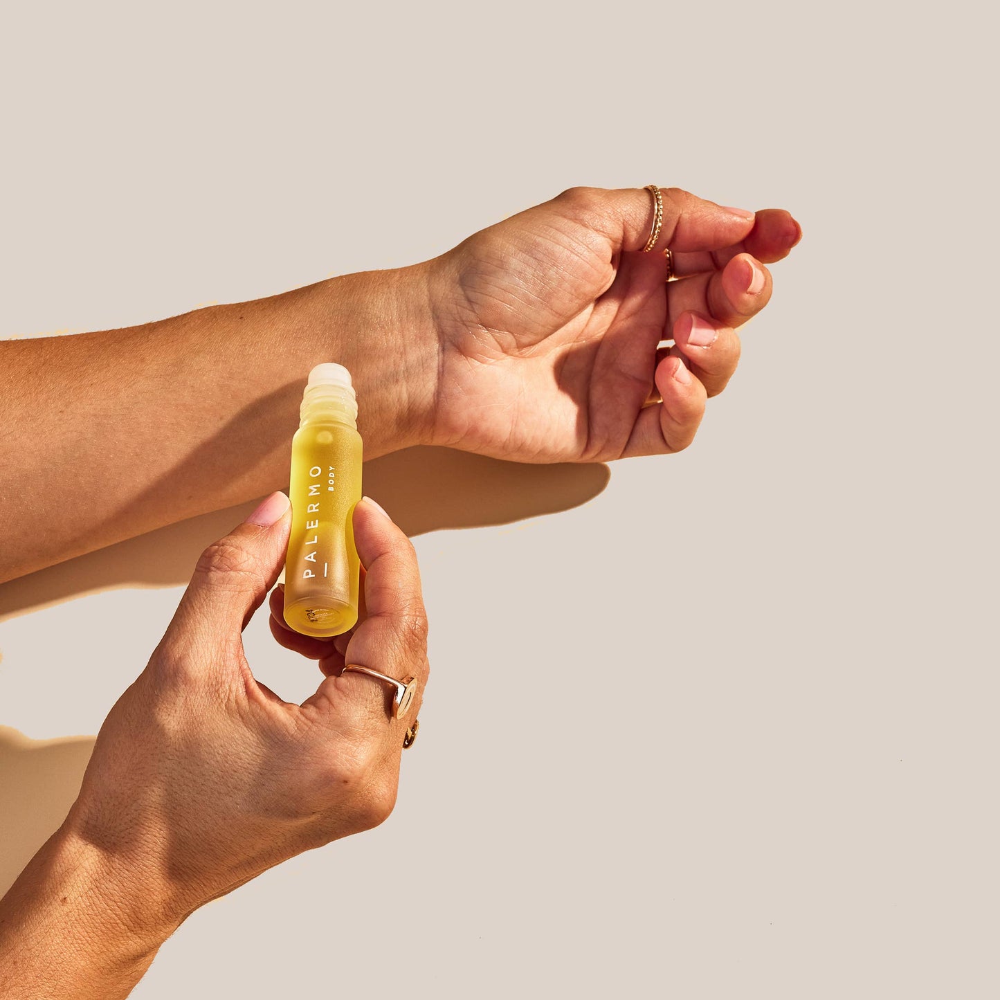 Hand holding a small bottle of the vitality aromatherapy oil acting as a natural perfume oil from Palermo body against a beige background