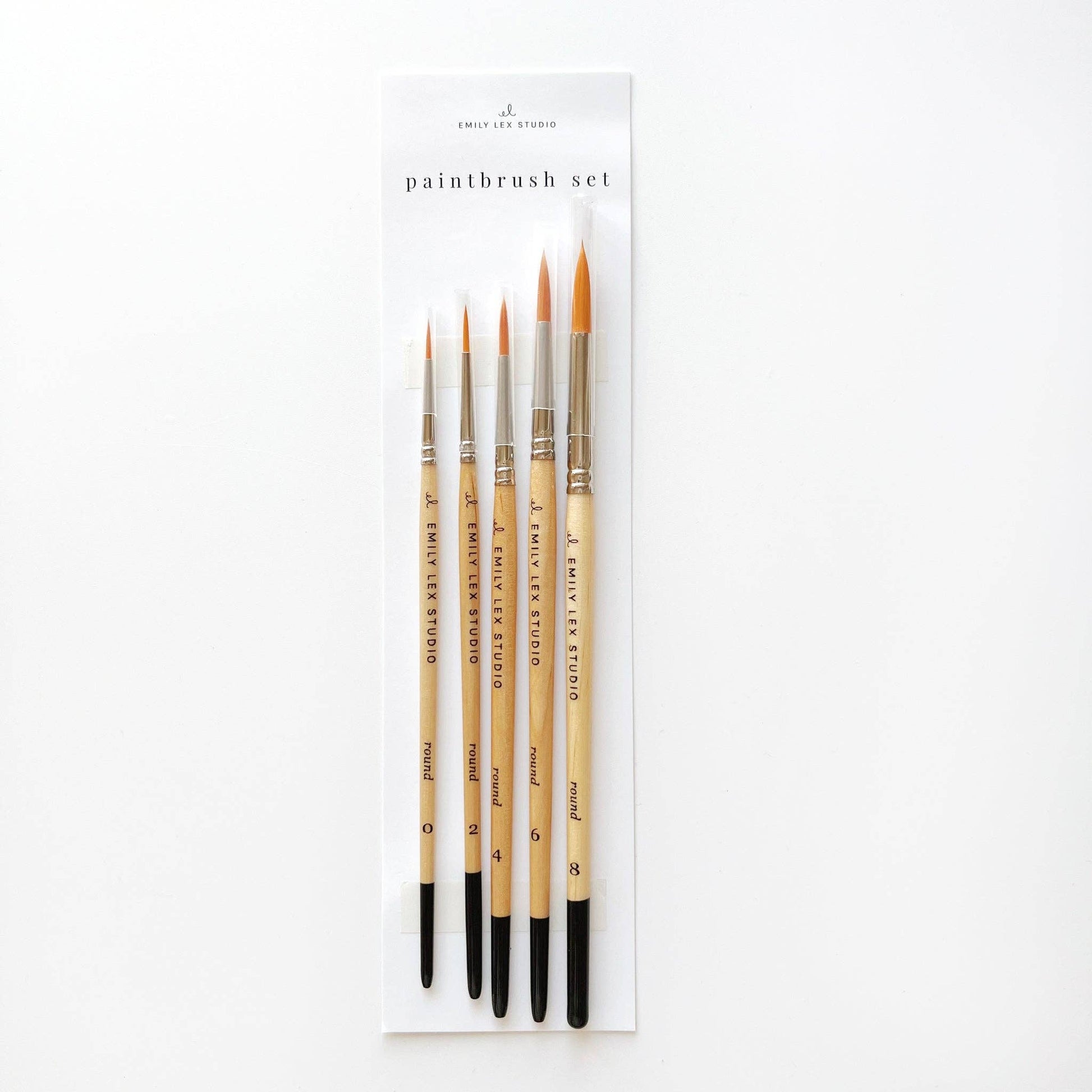 A set of five watercolor paintbrushes with golden synthetic taklon bristles, seamless aluminum ferrules, and lacquered wood handles, packaged in a clear plastic case with the label 'paintbrush set'.