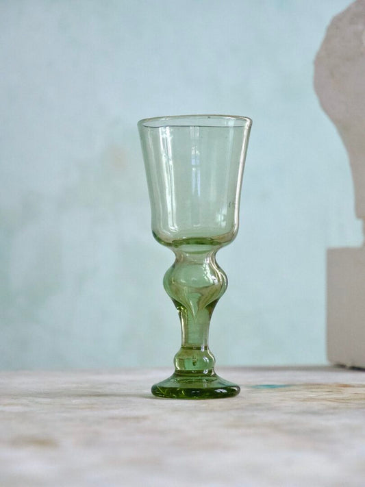 Green handmade French wine glass with visible stem on a light wooden surface with a neutral background