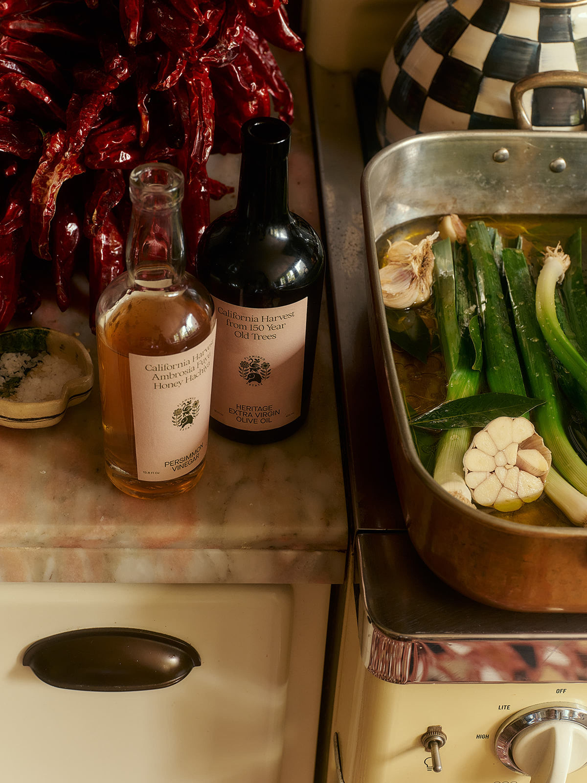Bottle of Persimmon vinegar and extra virgin oil on a stove next to a pan with vegetables.