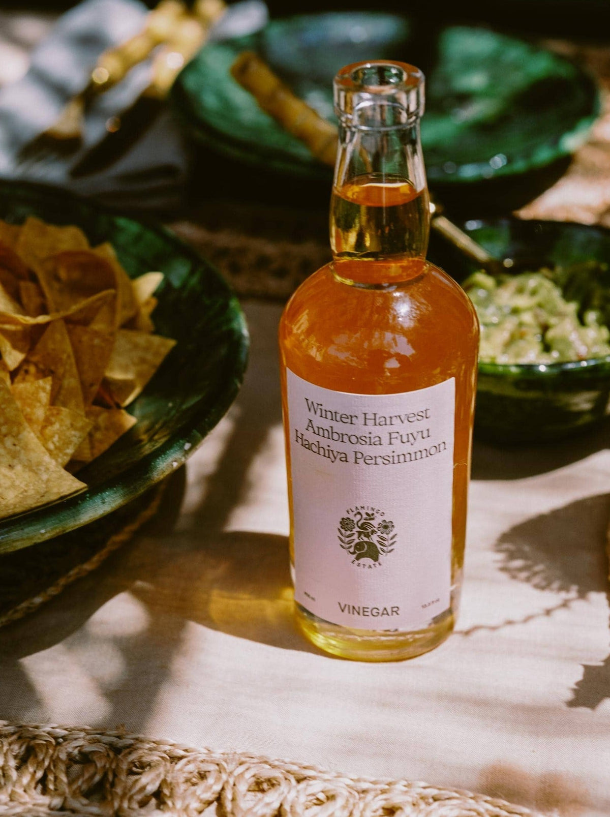 Bottle of Winter Harvest Persimmon vinegar, a sweet and tart Gourmet Fruit Vinegar on a table with chips and guacamole.