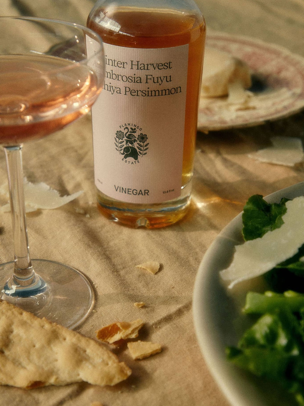 Bottle of 'Winter Harvest Ambrosia Fuyu' persimmon vinegar, a sweet and tart Gourmet Fruit Vinegar on a table with a glass of rose and food.